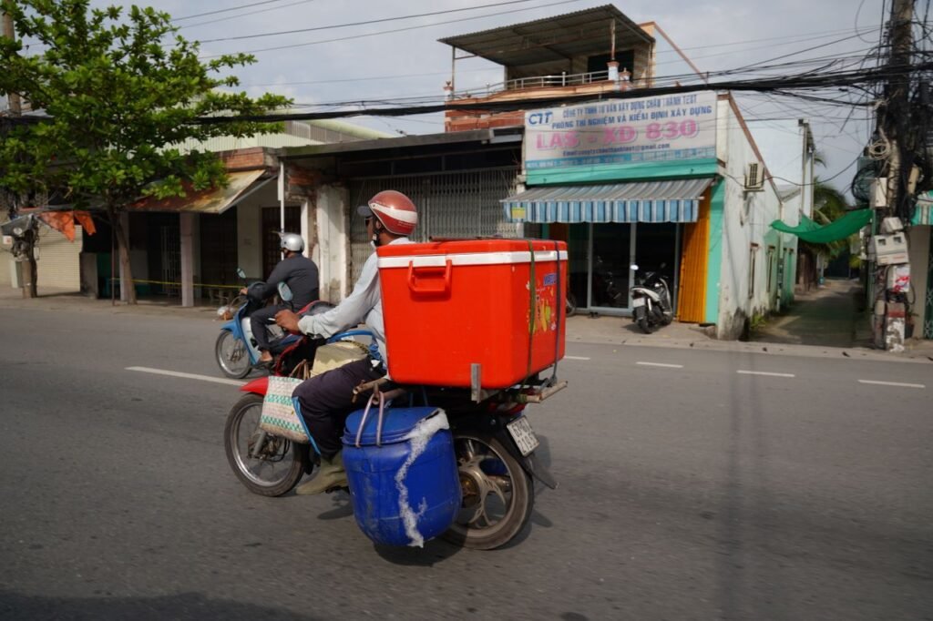 The Art of Drawing Readers In: Your attractive post title goes here A person riding a delivery motorcycle carrying a red container on an urban street.