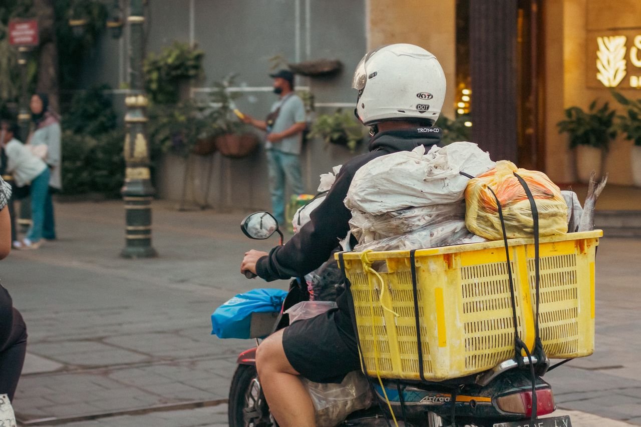 A man on a motorcycle transporting goods in a busy urban street scene.