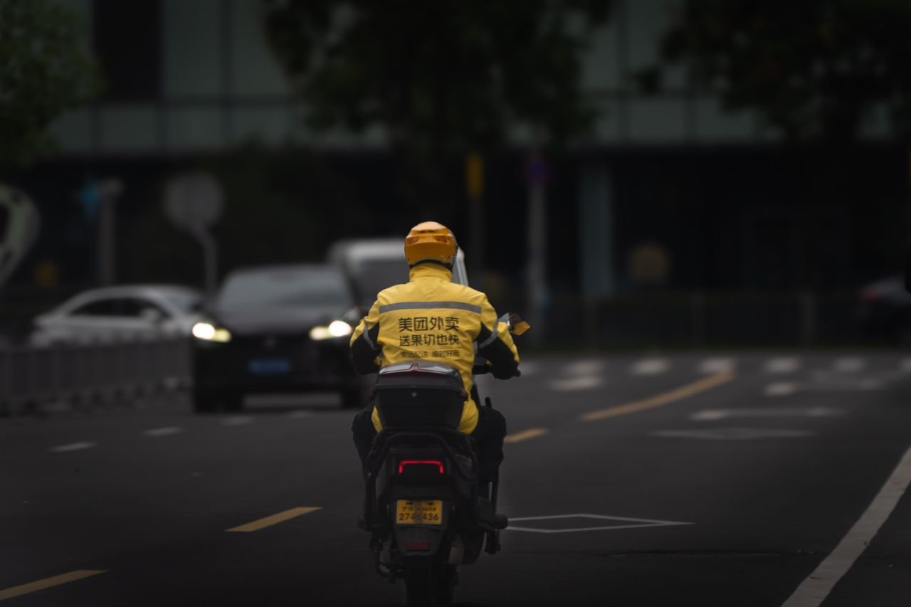 Urban delivery driver in yellow jacket on scooter navigating city streets.
