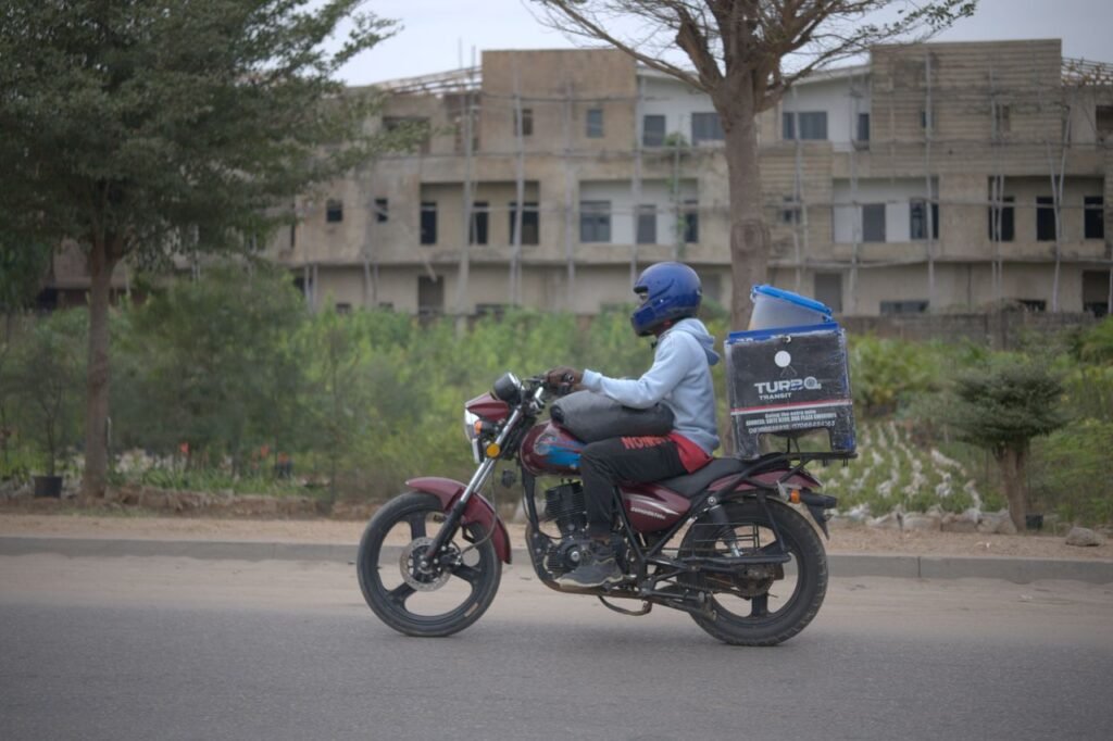Mastering the First Impression: Your intriguing post title goes here Motorcycle delivery rider with package box in urban Nigeria setting.
