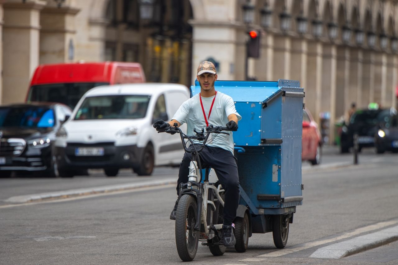 A courier rides a cargo bike in a busy street of Paris, showcasing urban delivery service.